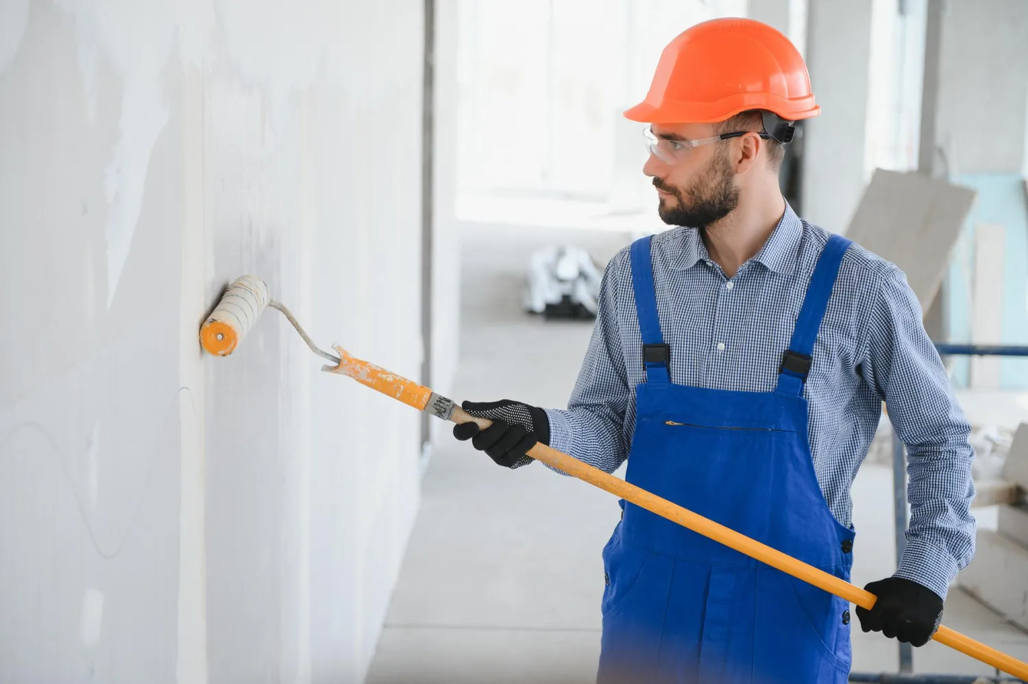 Painter using extension pole to paint white commercial hallway