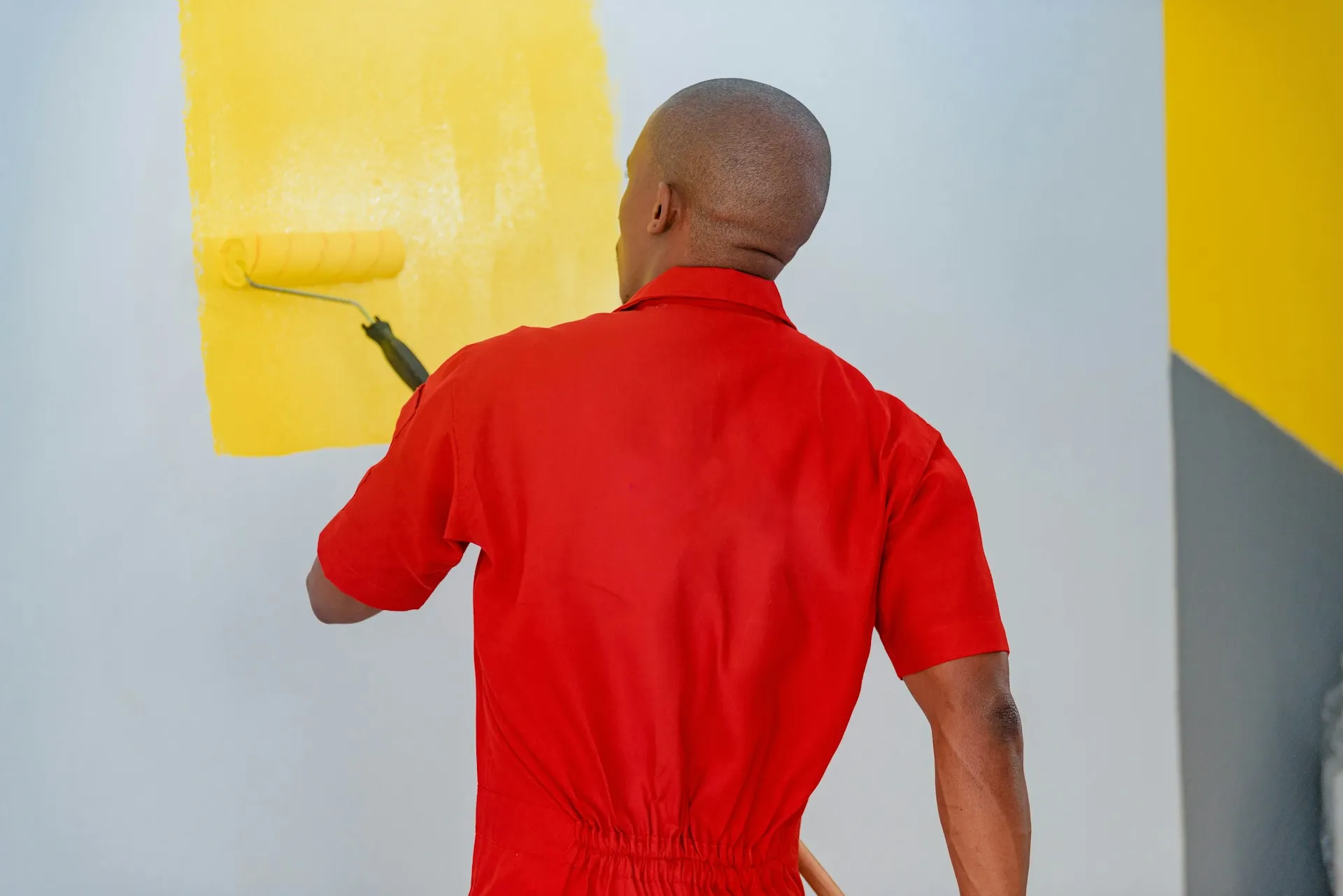 Painter in red shirt using roller on yellow wall