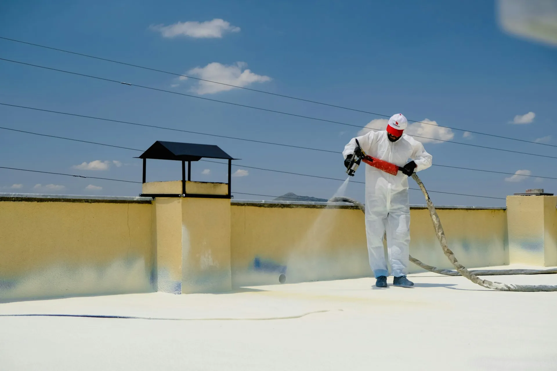 Worker spray coating commercial roof surface in protective suit