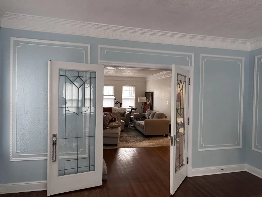Double doors open to a light-filled living room with beige furniture and a patterned rug.